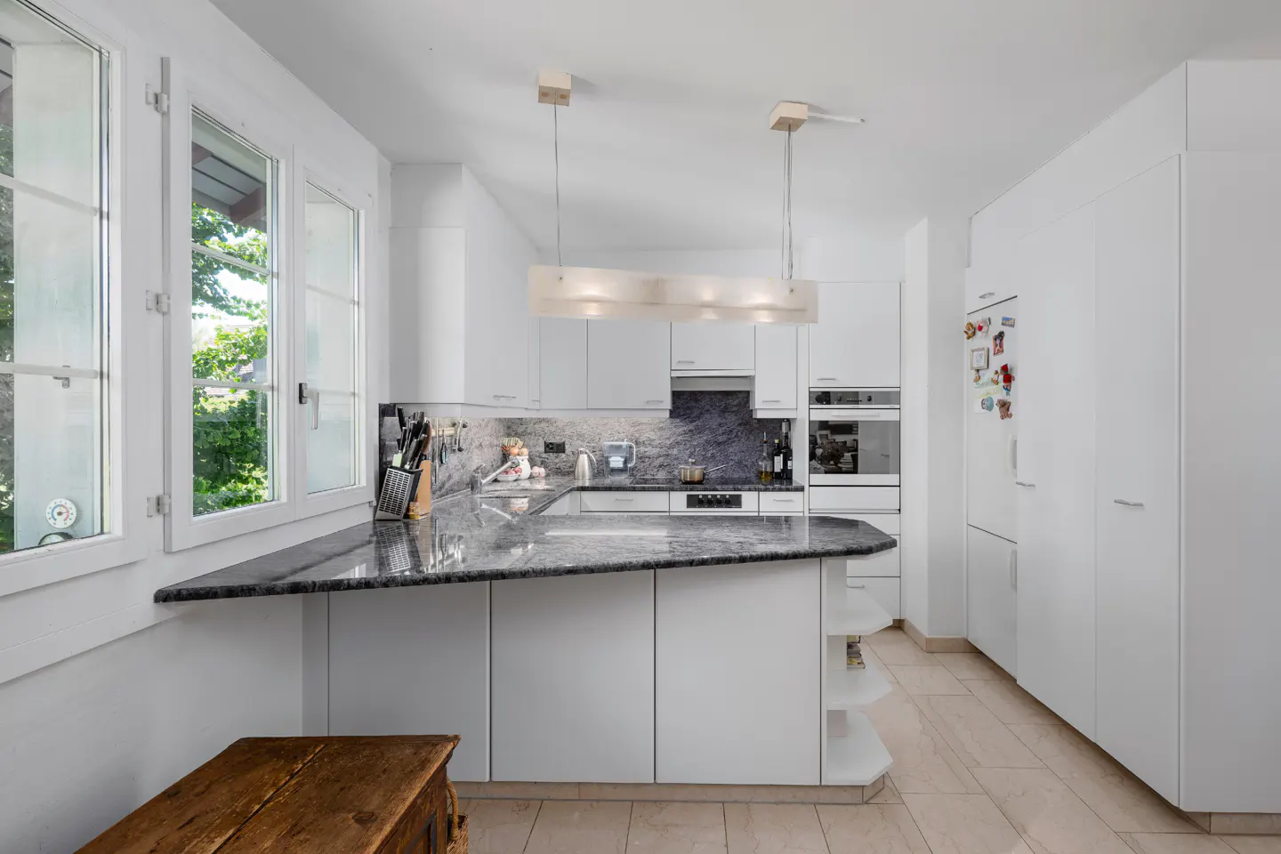 Bright, modern kitchen with white cabinets, granite countertops, and stainless steel appliances. A wooden chest sits near a window.