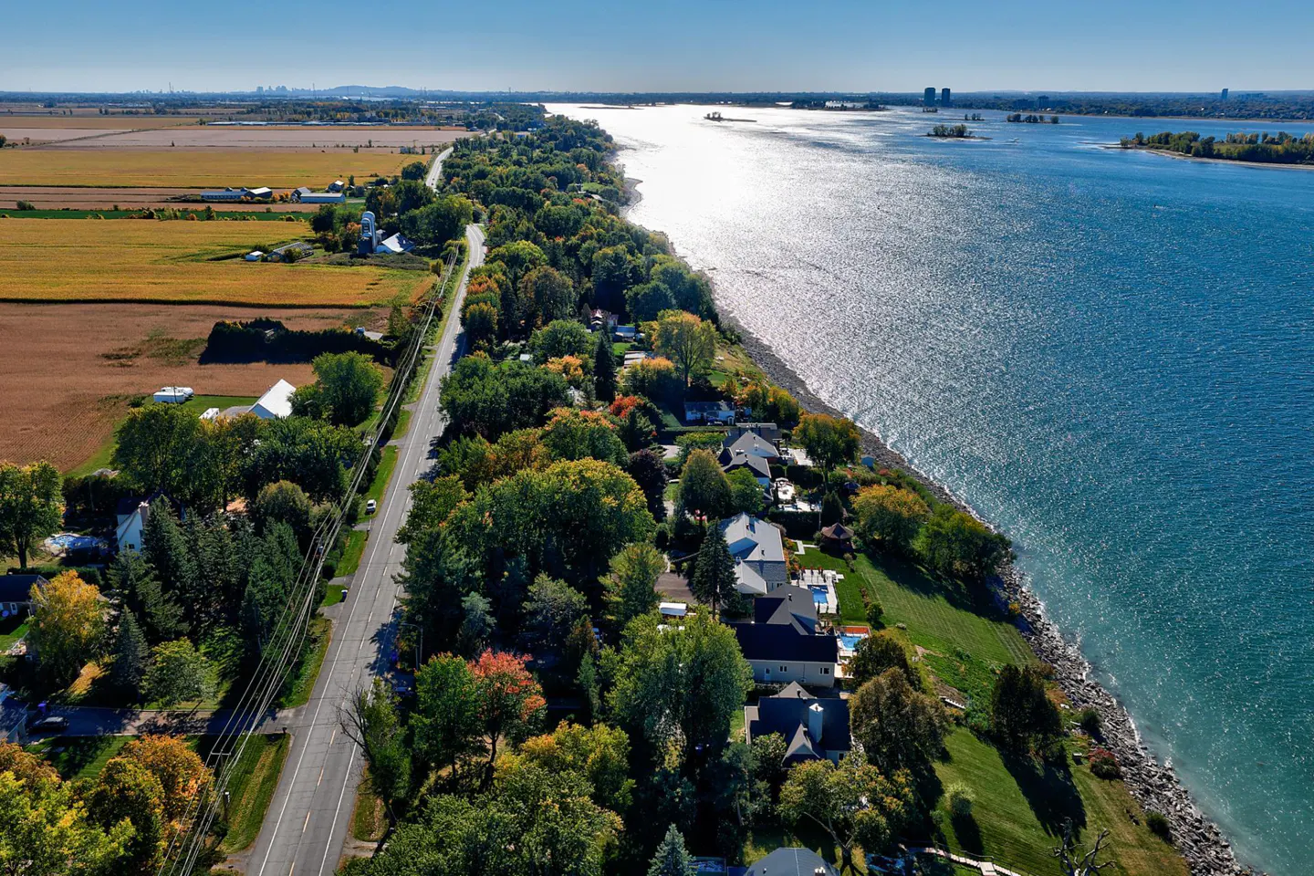 Aerial view of waterfront homes. A road runs between farmland and houses along a blue river.