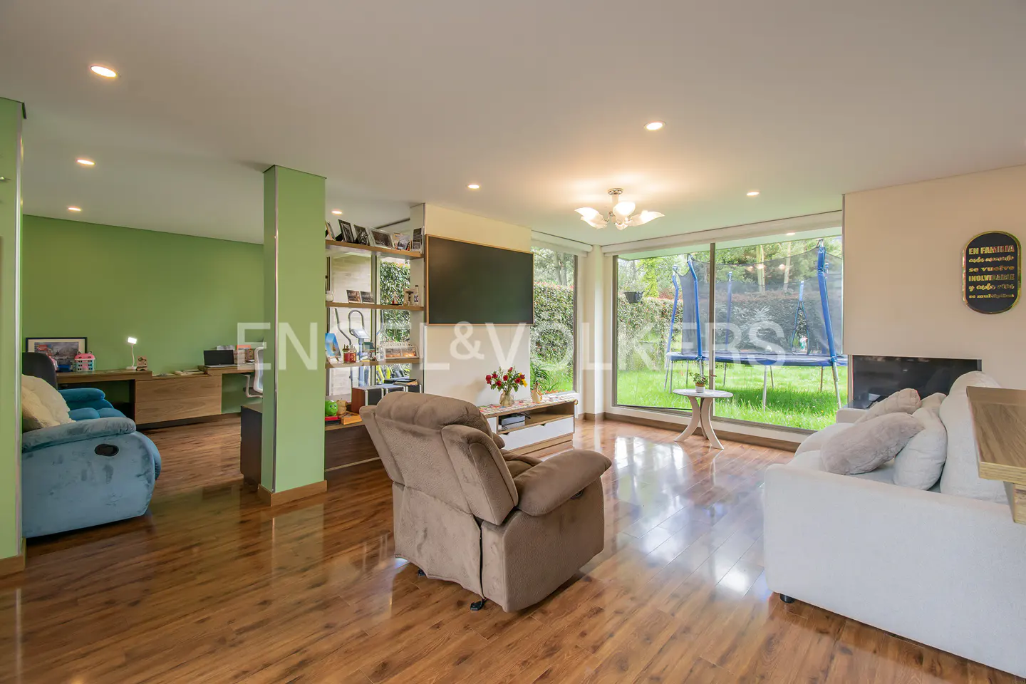 Living room with hardwood floors, a brown recliner, and a white sofa. A trampoline is visible through the large windows.
