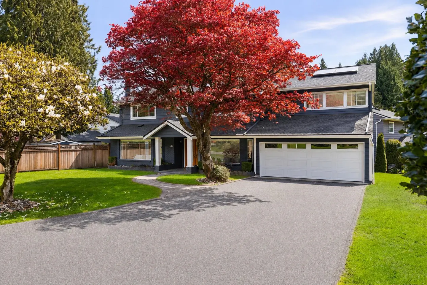 Two-story gray house with white trim, a white garage door, and a red tree in the front yard.