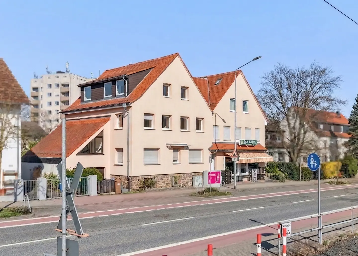 Two-story beige building with a red tile roof, street view, and pedestrian crossing sign.
