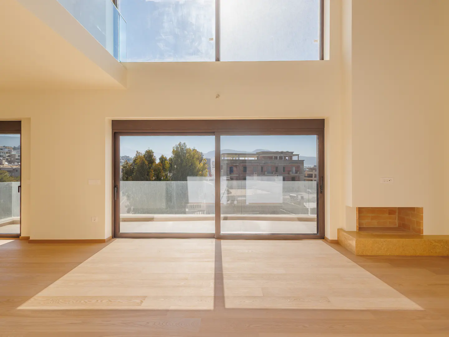 Bright, empty room with light wood floors, cream walls, and large sliding glass doors to a balcony with a city view.