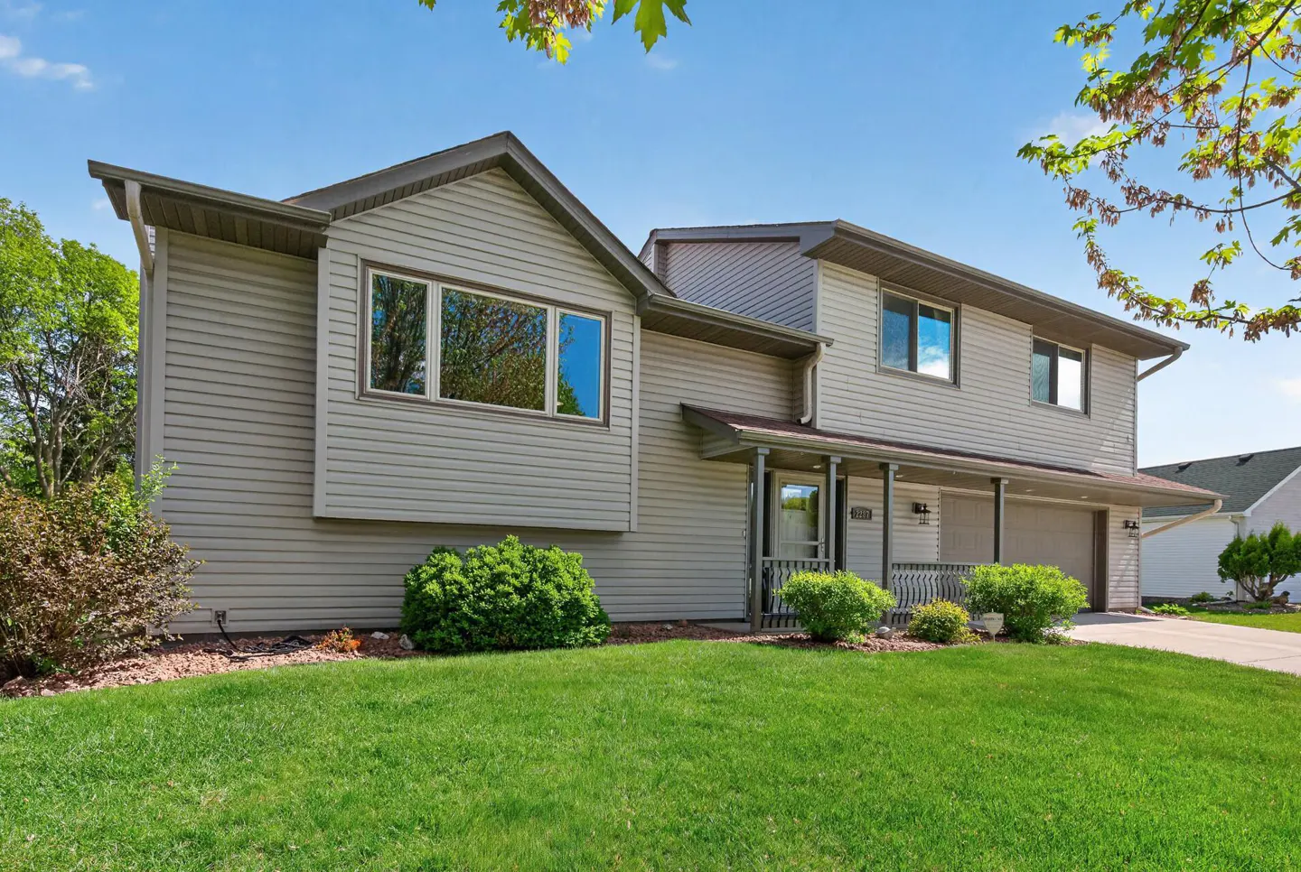 Two-story house with light-gray siding, a covered porch, and a green lawn on a sunny day.