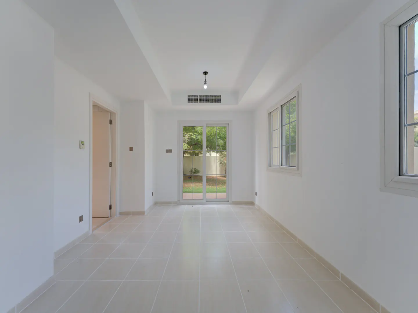 Bright, empty room with white walls, tile floor, and sliding glass doors to a green yard. Windows let in natural light.