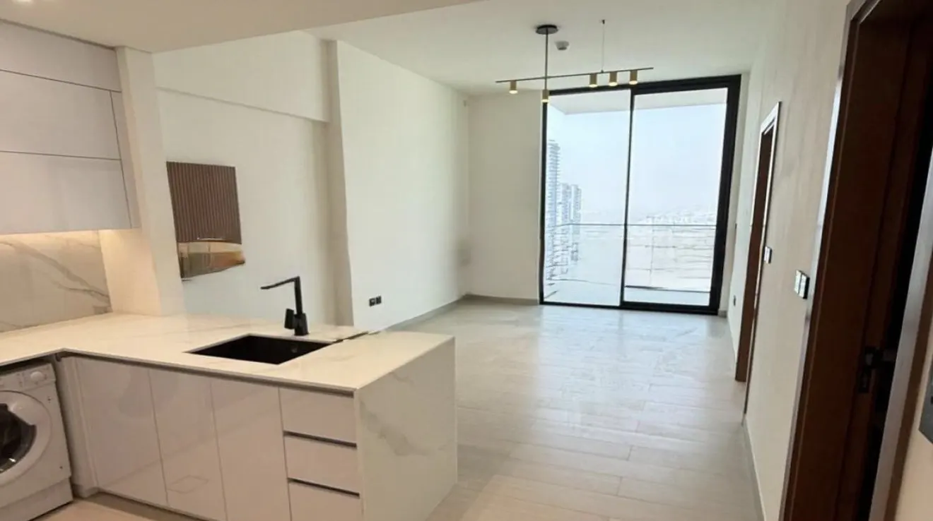 A bright, modern apartment interior with white cabinets, a black sink, and a sliding glass door leading to a city view.