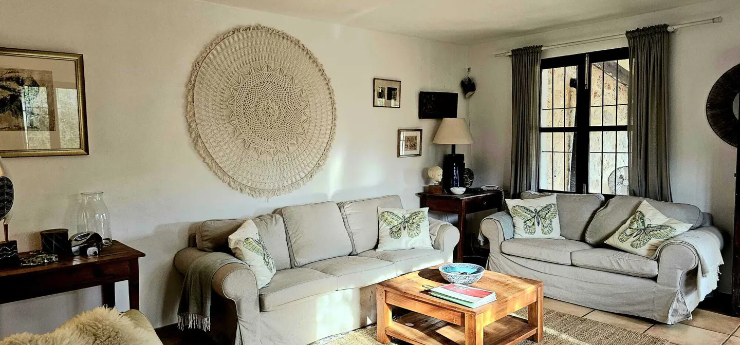 Cozy living room with beige sofas, butterfly pillows, a large circular macramé wall hanging, and a wooden coffee table.
