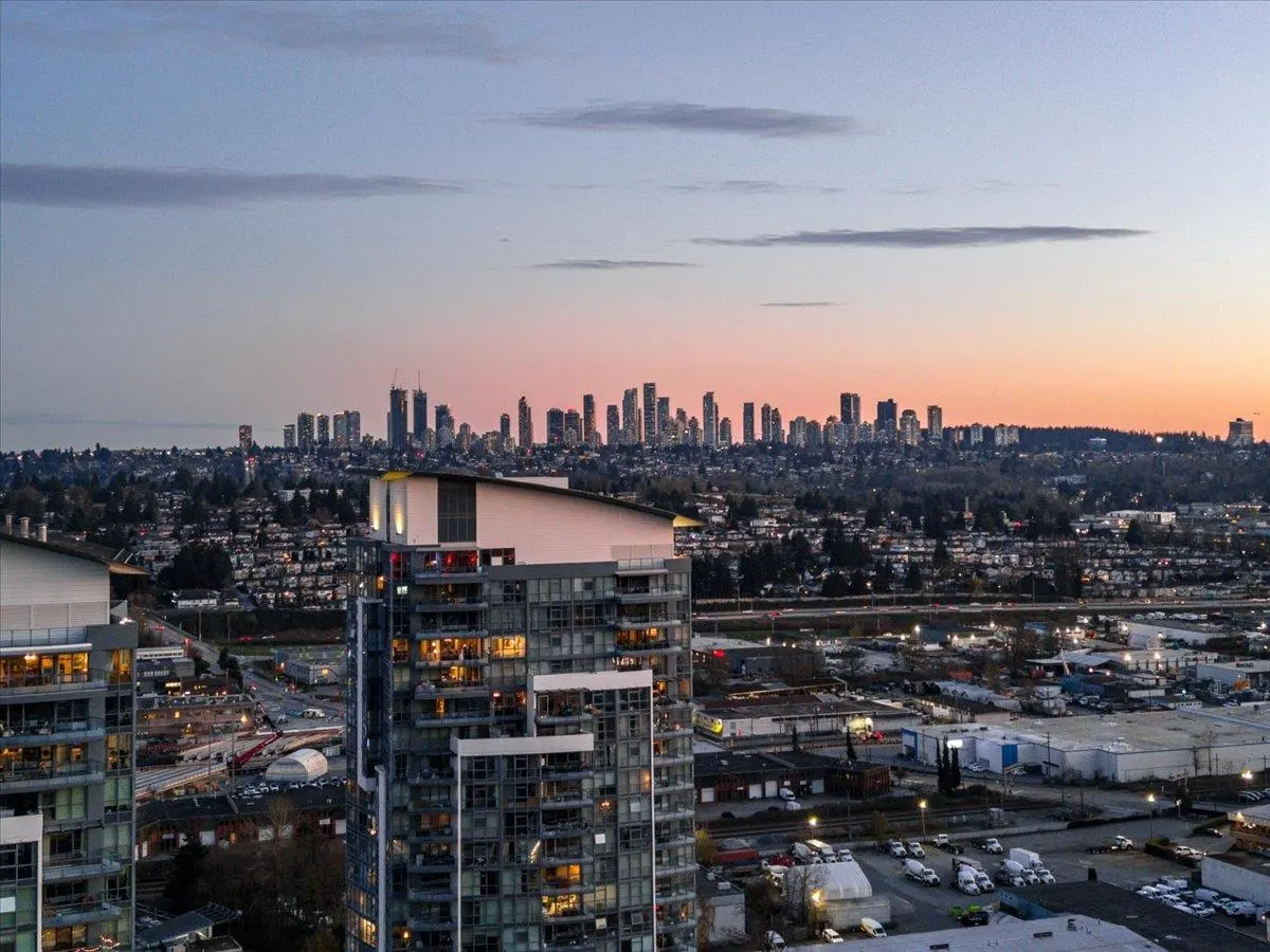 Cityscape view at dusk featuring modern high-rise buildings with illuminated windows, set against a skyline with a pink-tinged sky.