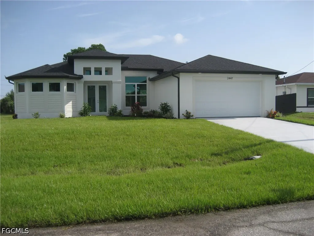 Single-story white modern home with a dark roof, two-car garage, and a large green lawn under a clear blue sky.