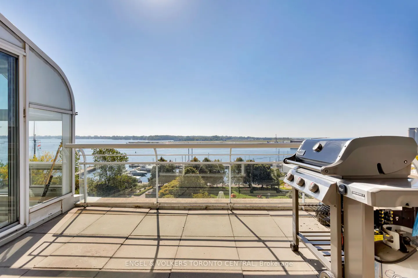 Condo balcony with a stainless steel grill, glass railing, and a view of the water and boats under a clear blue sky.