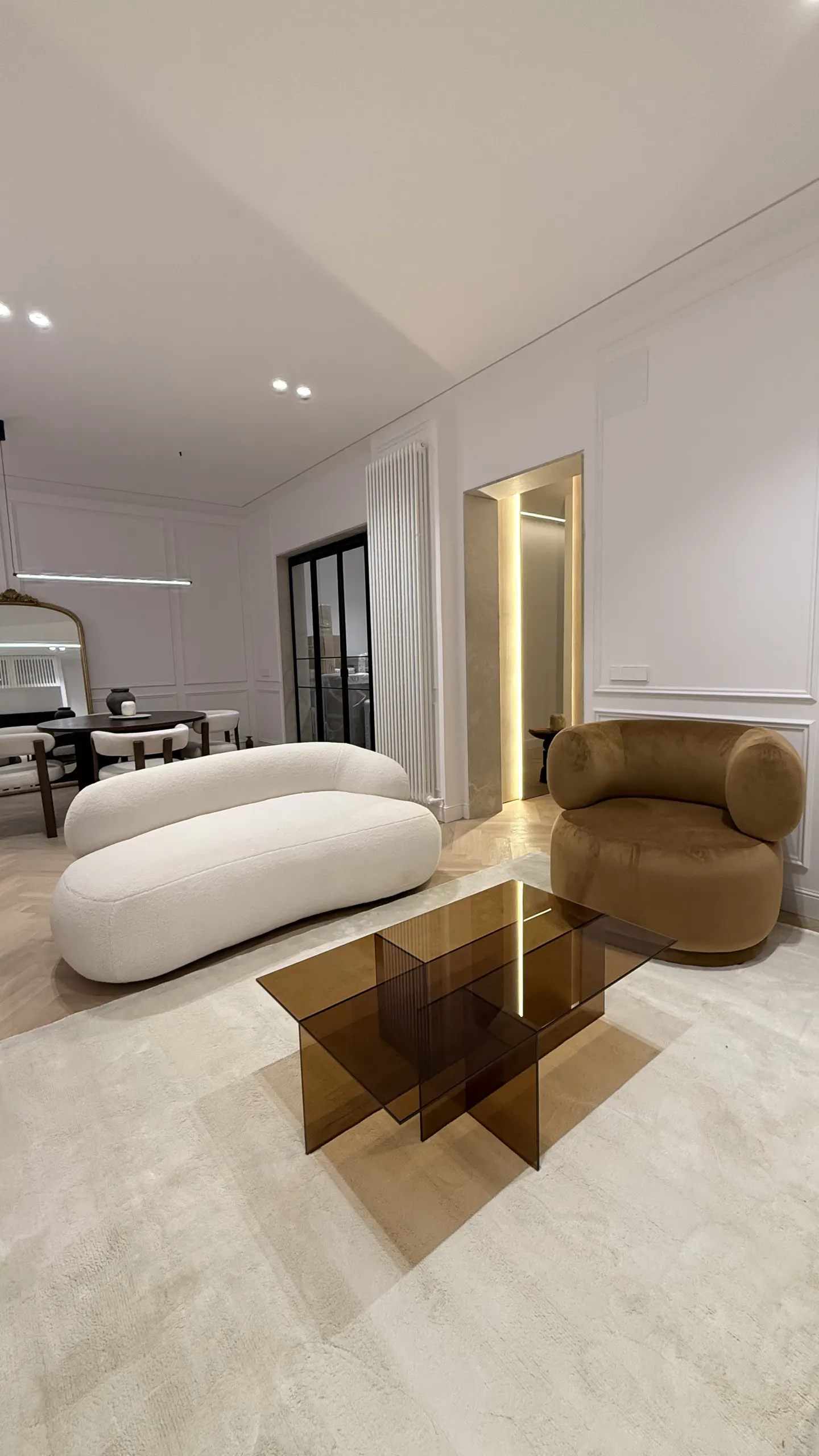 Modern living room with a white curved sofa, brown velvet loveseat, and a translucent amber glass coffee table.