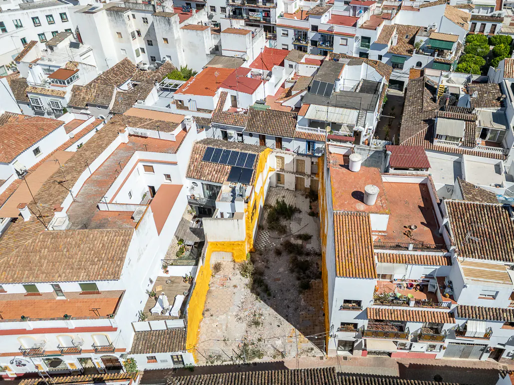 Aerial view of a vacant lot surrounded by white buildings with terracotta roofs in a dense urban area.