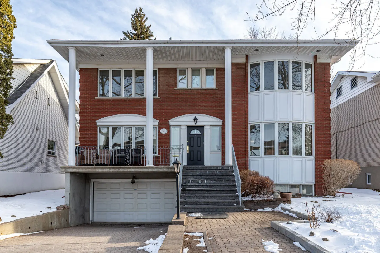 Two-story red brick house with white columns, a black front door, and a garage. Snow is on the ground.