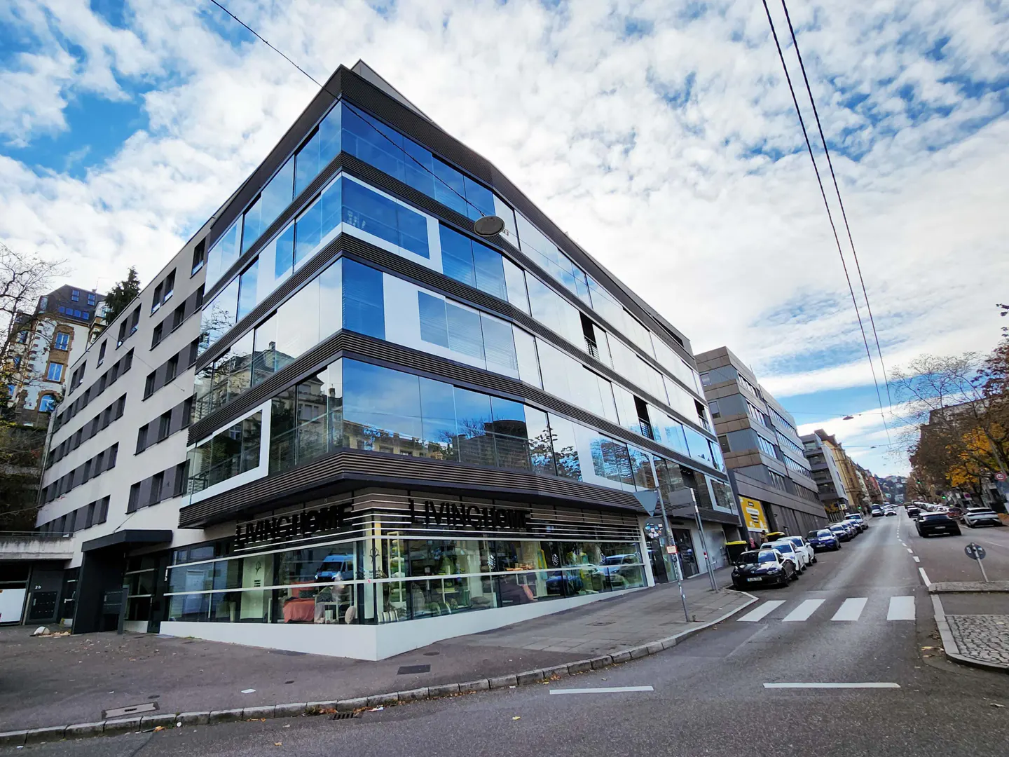 Modern building with glass facade and "LIVINGHOME" sign on the ground floor, street view with parked cars.