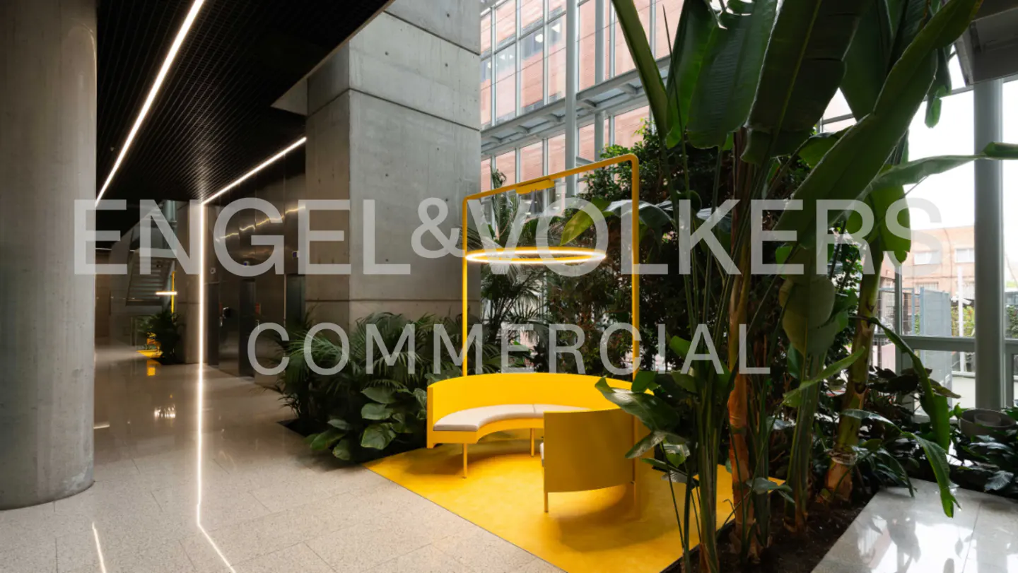 Modern office lobby with a yellow seating area, plants, and concrete pillars.