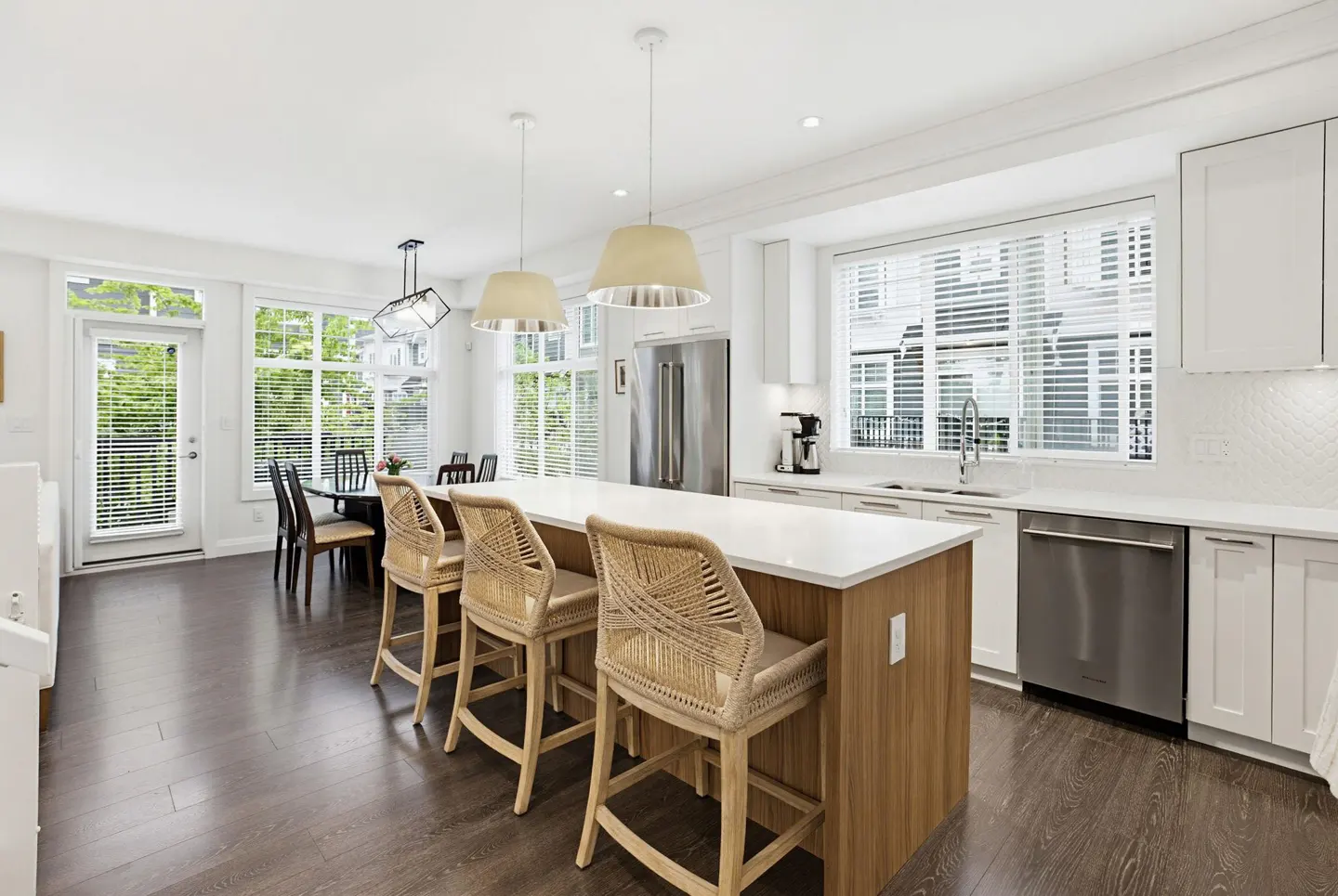 Bright, modern kitchen with white cabinets, stainless steel appliances, and a wood-paneled island with three woven bar stools.