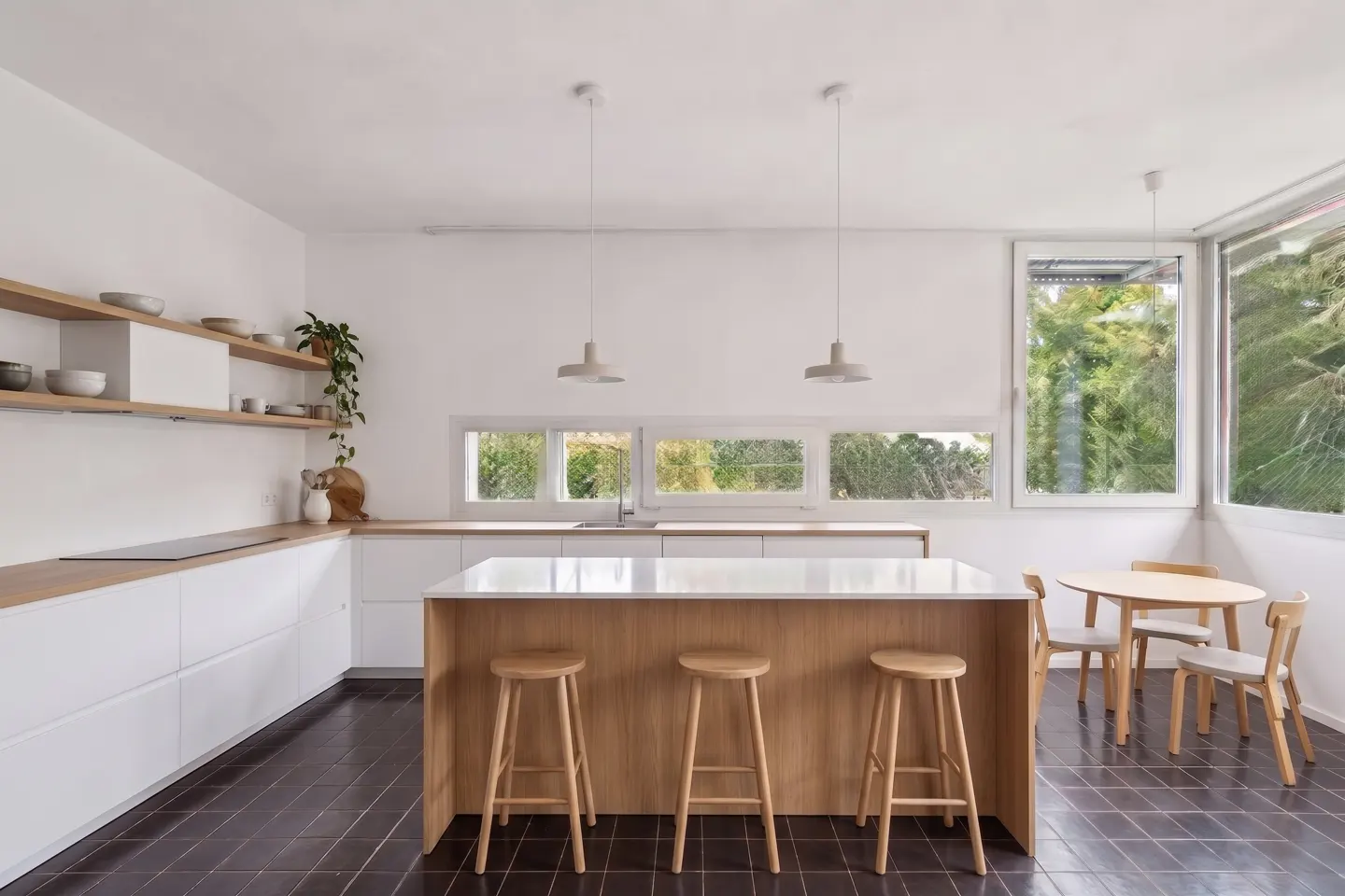 Bright kitchen with white cabinets, wood counters, and island with stools. Large windows offer a view of greenery. Round table and chairs nearby.
