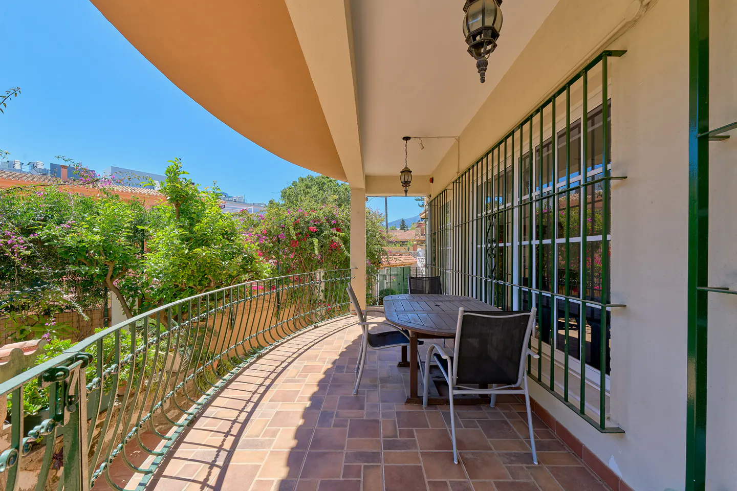 Outdoor patio with a table and chairs, a curved railing, and lush greenery in the background.