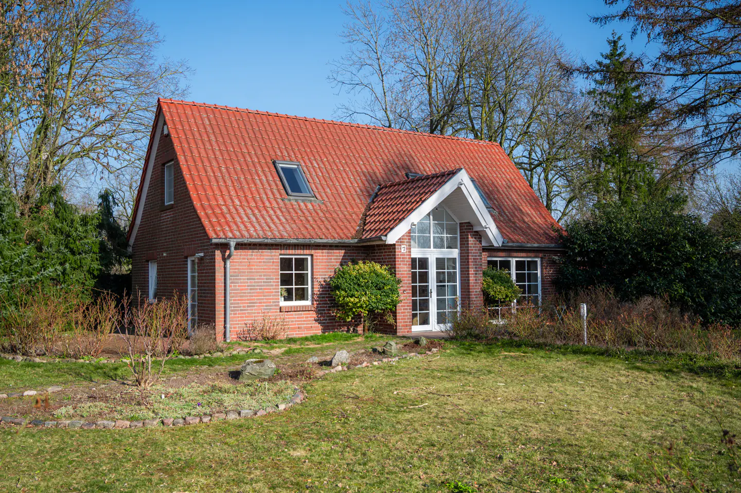 A single-story brick house with a red tile roof and white trim on a green lawn. Trees are in the background.