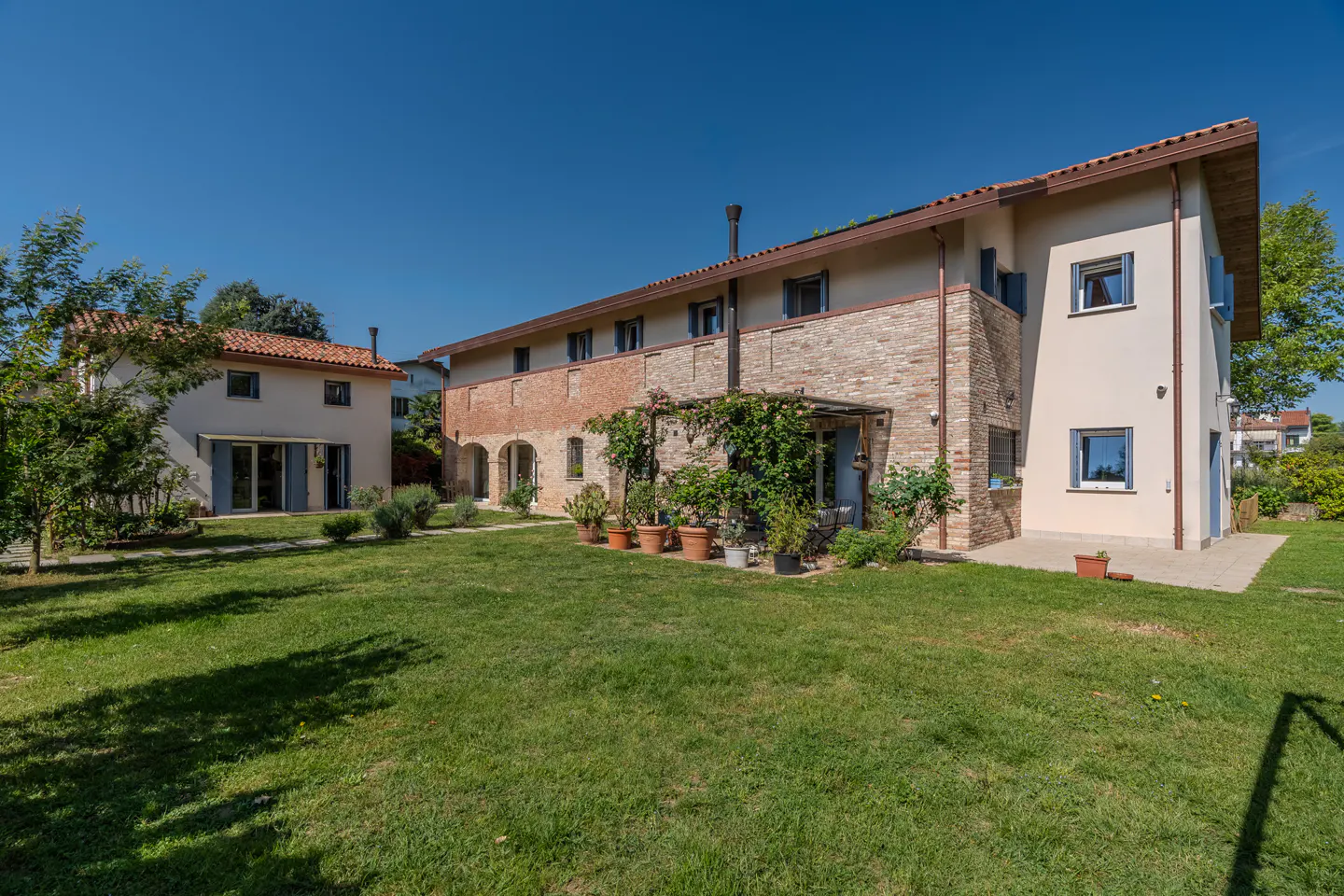 Exterior view of a two-story house with a brick facade and a green lawn under a clear blue sky.