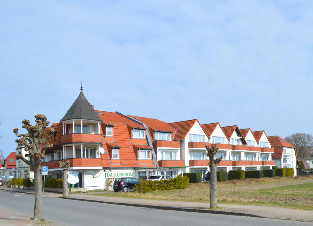 "Haus Usedom" building with red roof and black turret, seen from the street on a sunny day.