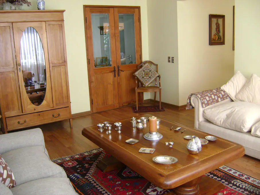 Living room with wood floors, a large wood armoire, and a wood coffee table with silver objects. A white sofa and wood-framed glass doors are also visible.
