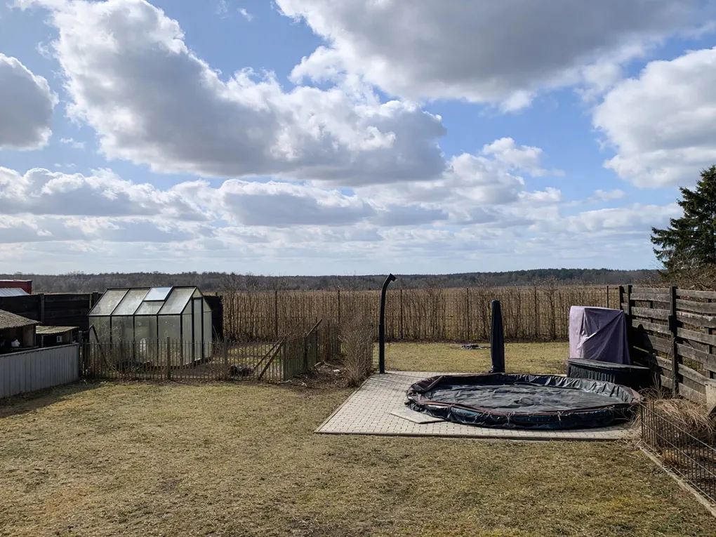 Backyard with a greenhouse, hot tub, and wooden fence under a cloudy sky.