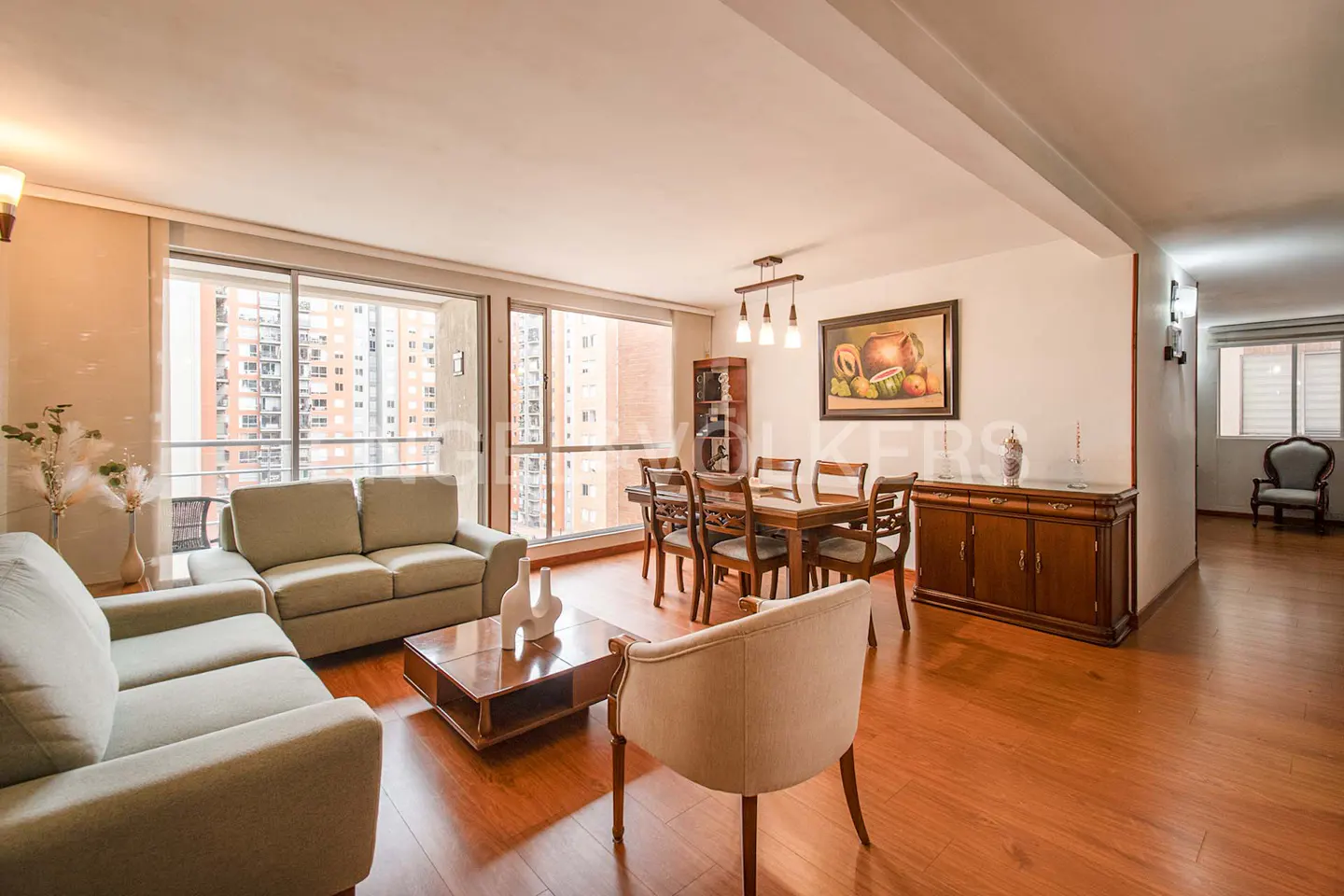 Bright, open-plan living and dining area with wood floors. Sofas, dining table, and city views through large windows.