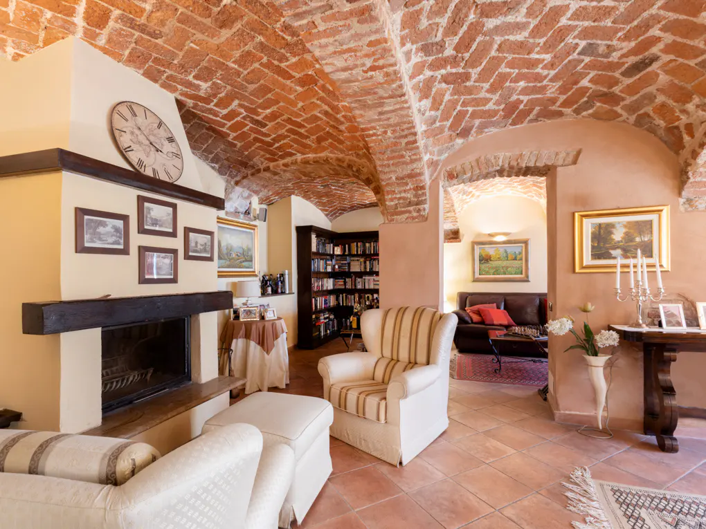 Living room with brick vaulted ceiling, fireplace, and striped armchairs. Paintings and a bookcase add to the room's charm.