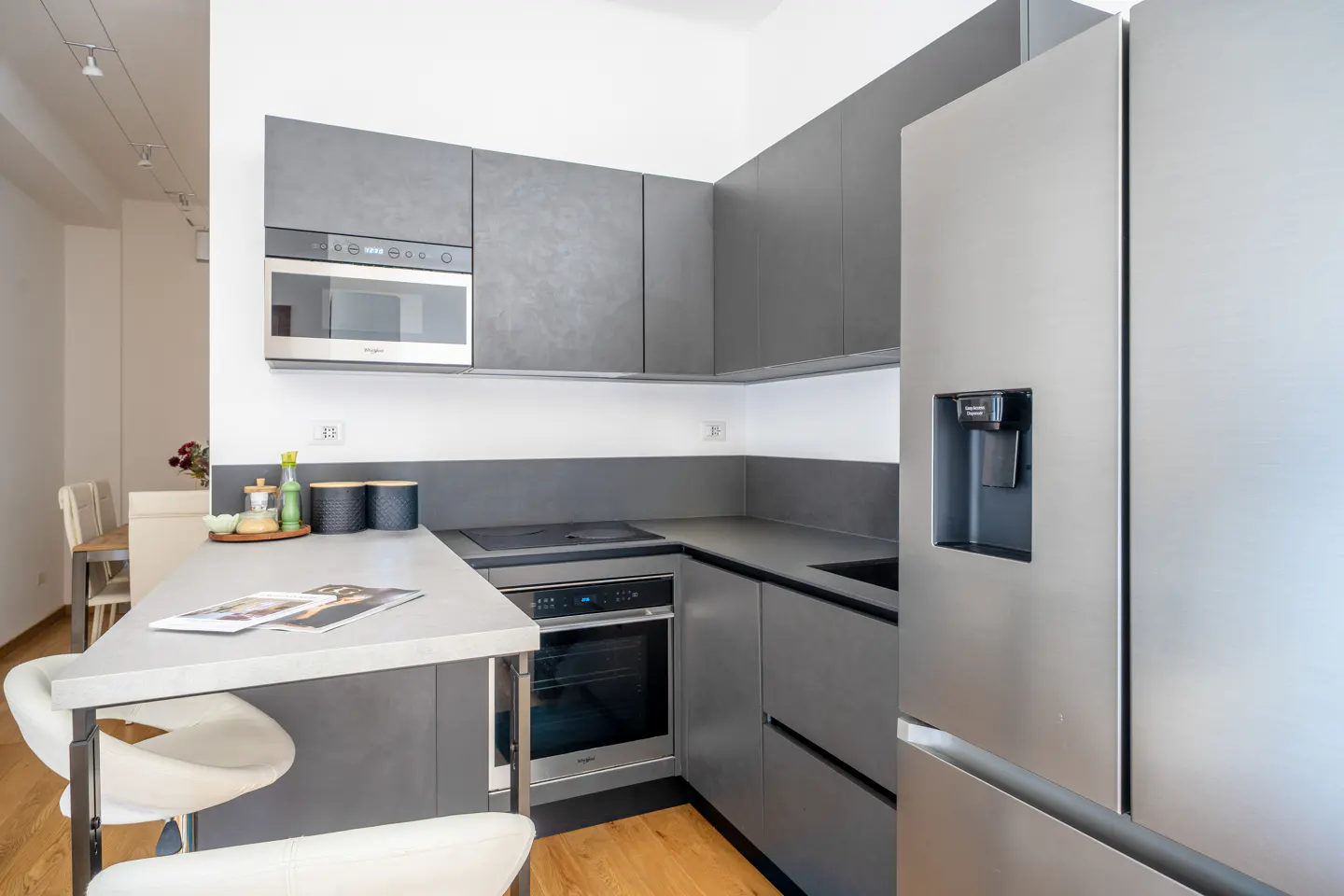 A modern kitchen with gray cabinets, stainless steel appliances, and a breakfast bar with white stools.