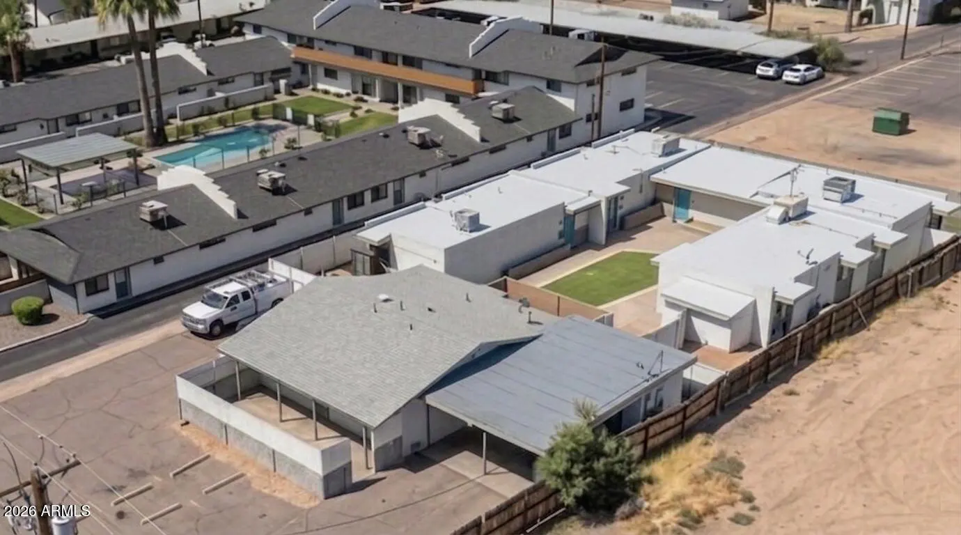 Aerial view of a white apartment complex with a pool, parking lot, and desert landscape.