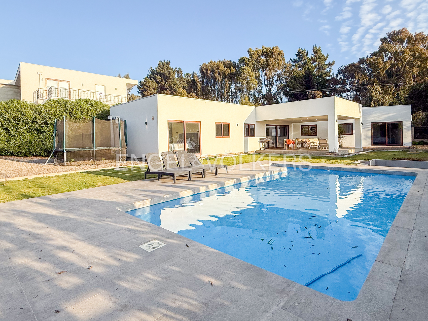 Modern white house with a swimming pool, patio lounge chairs, a trampoline, and a covered outdoor dining area. [AI-generated text]