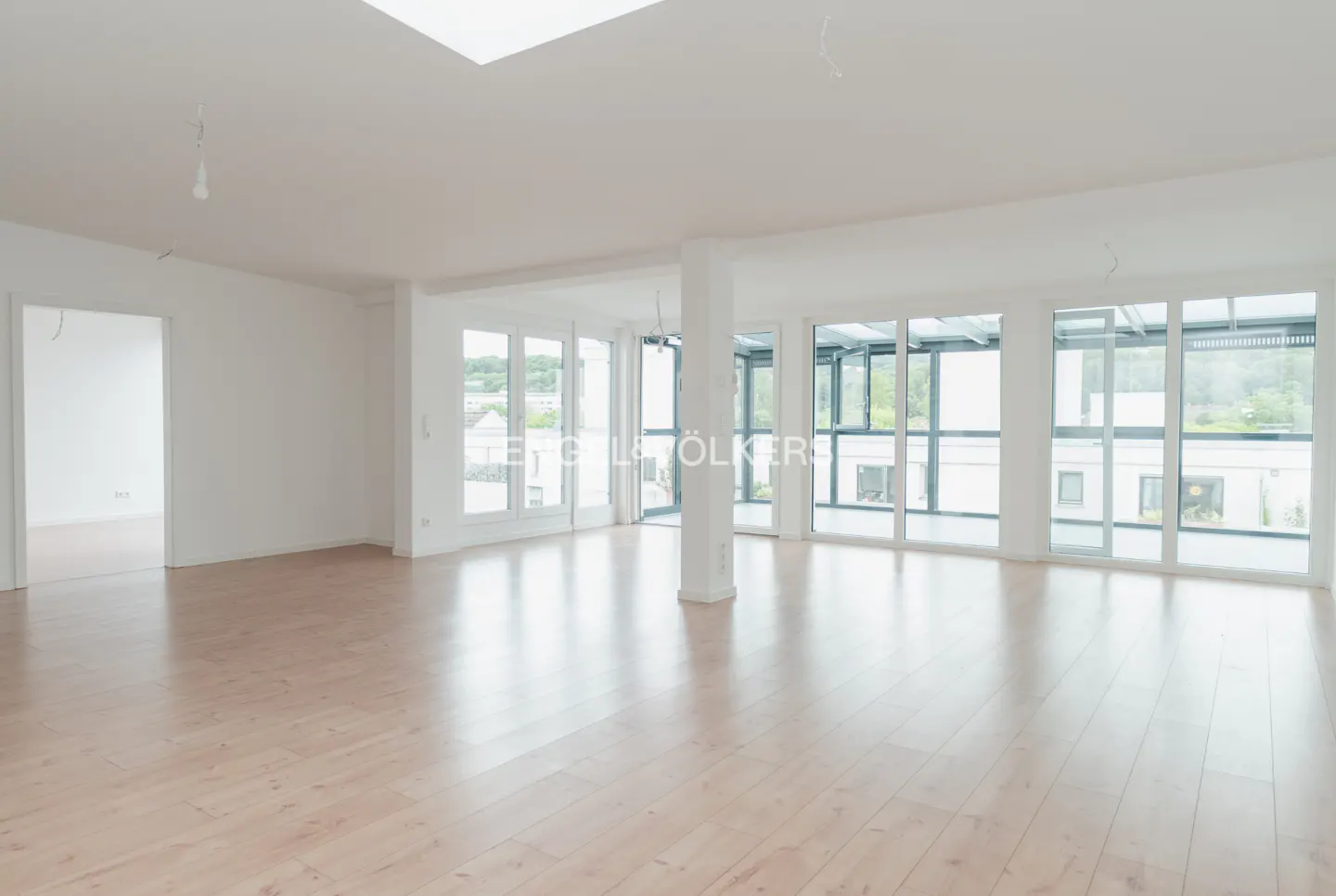 Bright, spacious, unfurnished room with light wood floors, white walls, and large floor-to-ceiling windows.