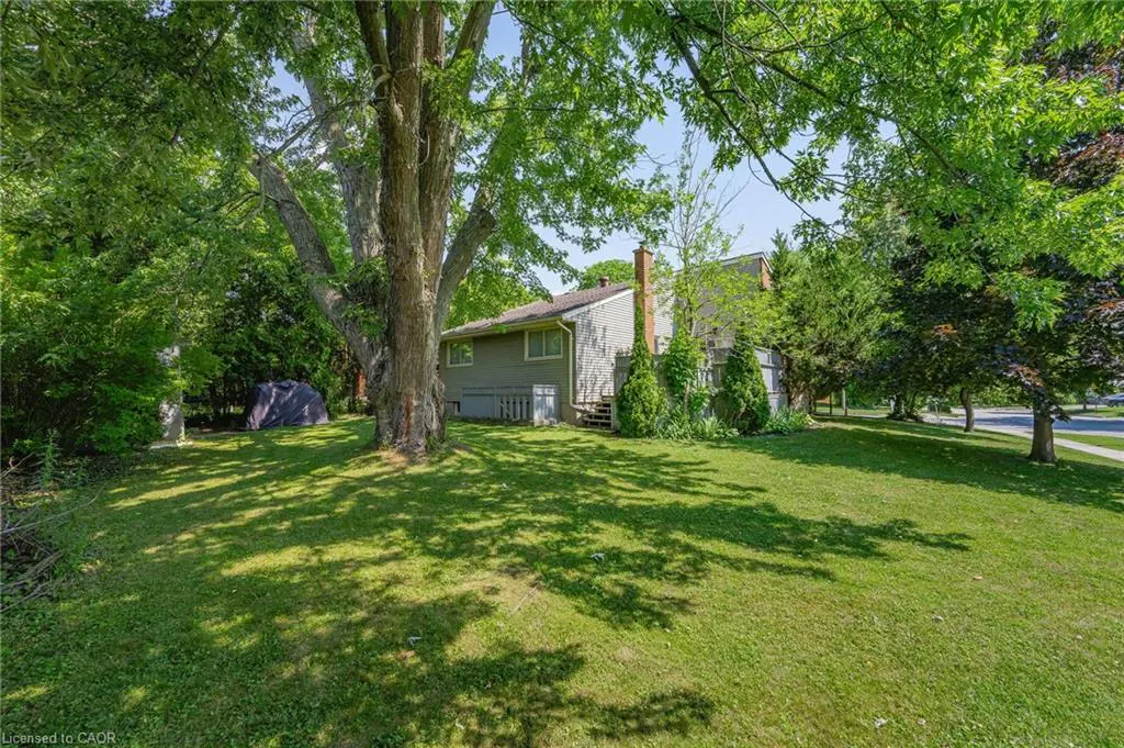 Exterior view of a two-story house with gray siding, a brick chimney, and a large green lawn with trees.