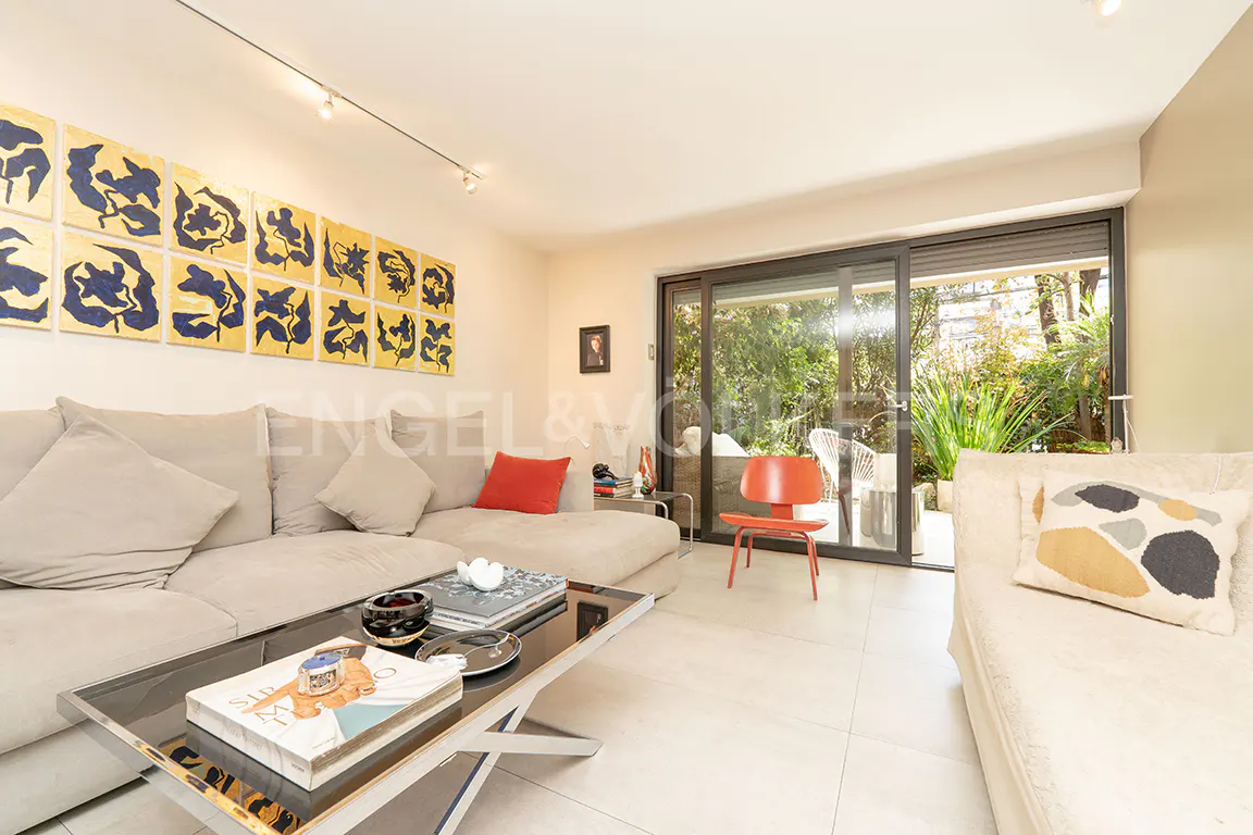 Living room with beige sectional sofa, black coffee table, and orange chair near sliding glass doors to a patio with greenery.