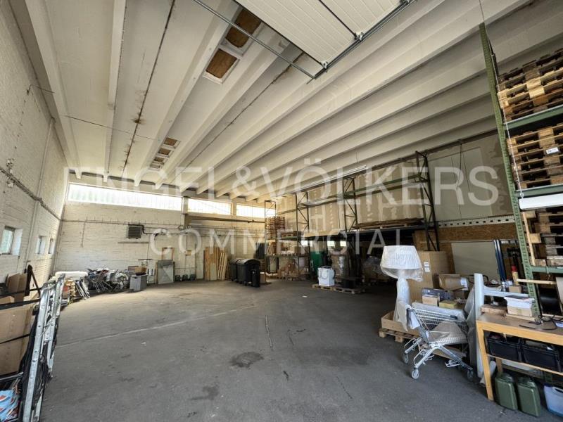 Spacious industrial warehouse with high ceilings, concrete floors, metal storage racks, and scattered equipment. [AI-generated text]