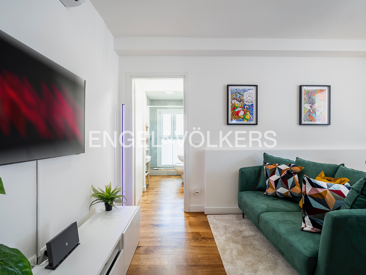Modern living room with a green velvet sofa, patterned pillows, wall art, and a view into a bright bathroom. [AI-generated text]