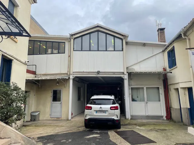 A white Citroen SUV is parked in a garage of a two-story building with white siding and black-framed windows.