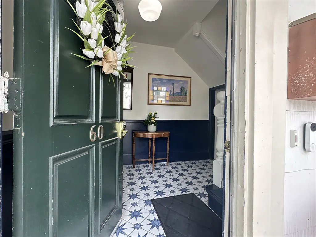Open dark green front door with a white tulip wreath, revealing a foyer with blue and white star-patterned tile flooring.