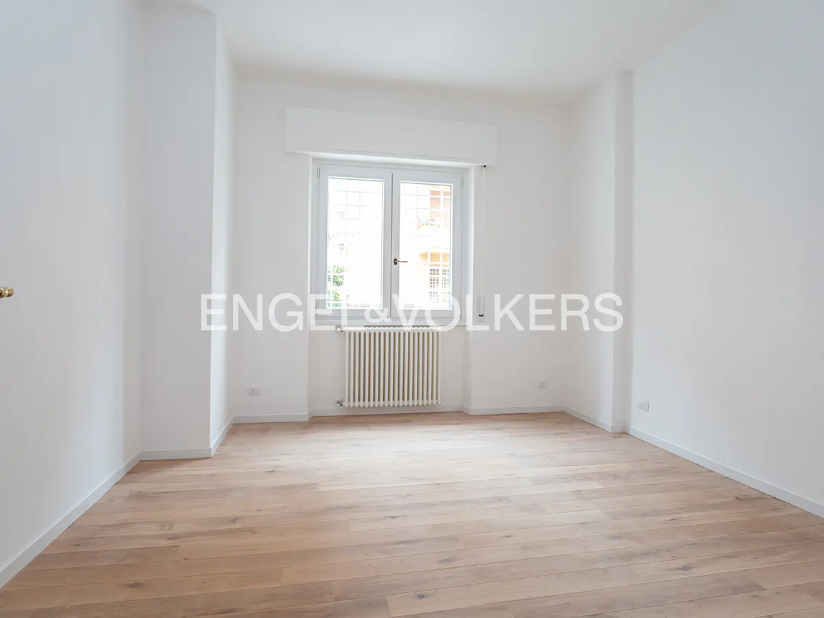 Bright, empty room with white walls, light wood floors, and a window with a radiator below.