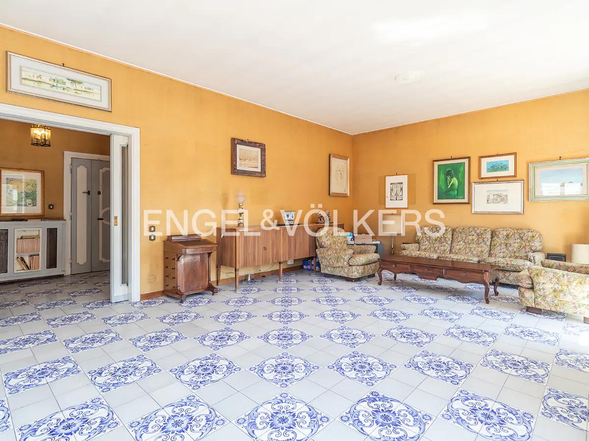 A living room with yellow walls, floral furniture, and blue and white patterned tile flooring. Artwork hangs on the walls.