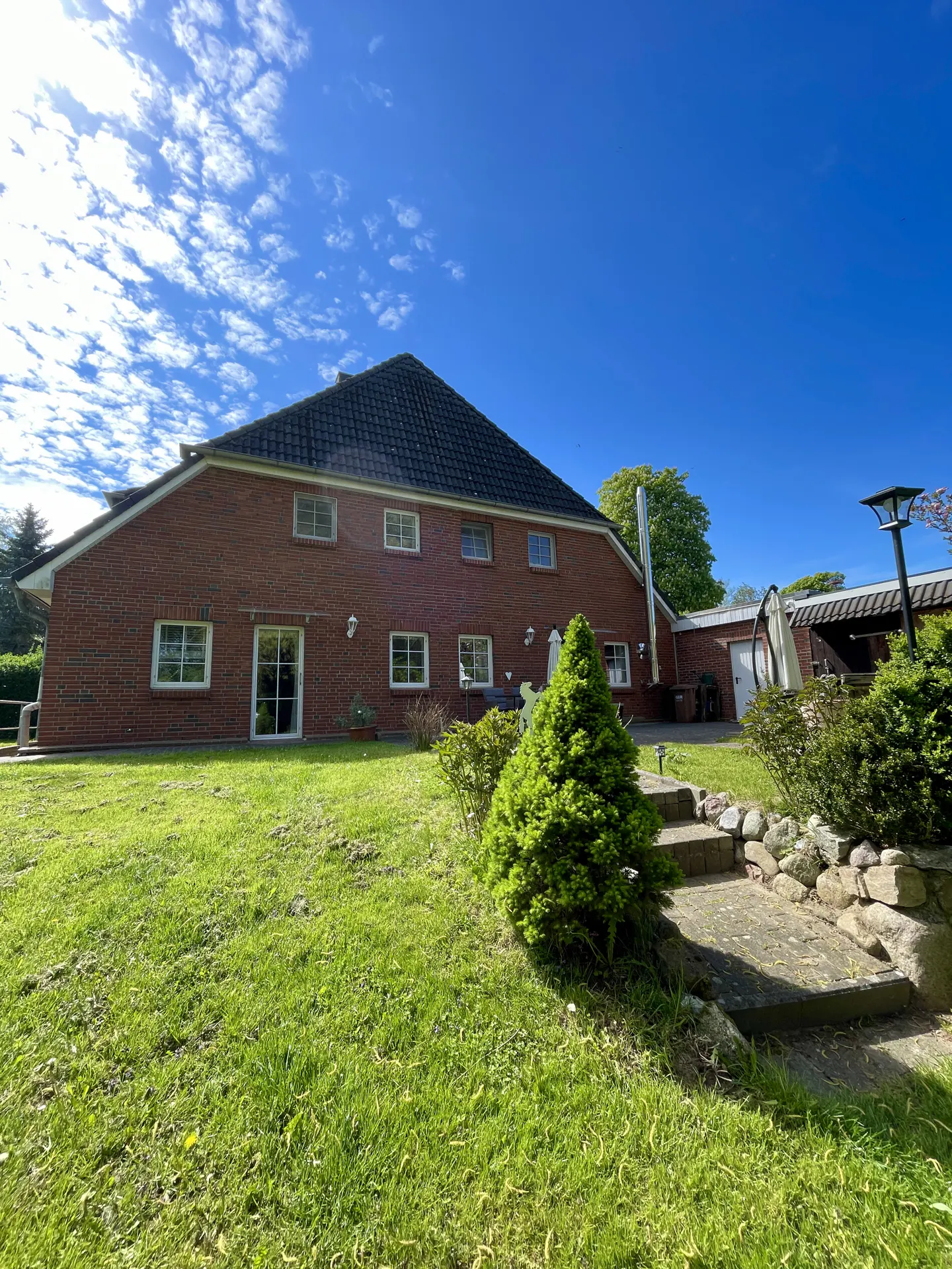 Backyard view of a two-story red brick house with a black roof, green lawn, and blue sky.