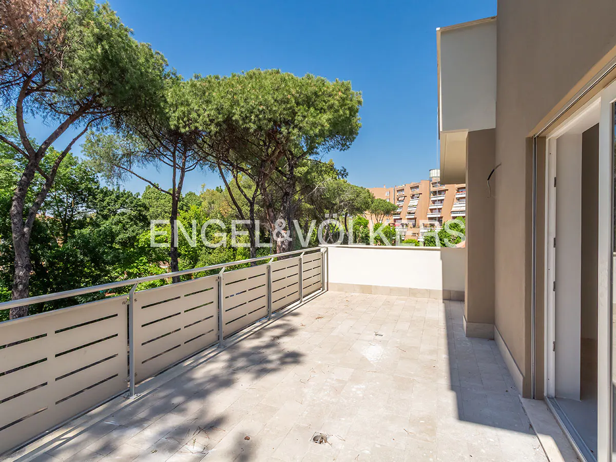 Spacious beige balcony with a modern metal railing, overlooking lush green trees and a distant apartment building.