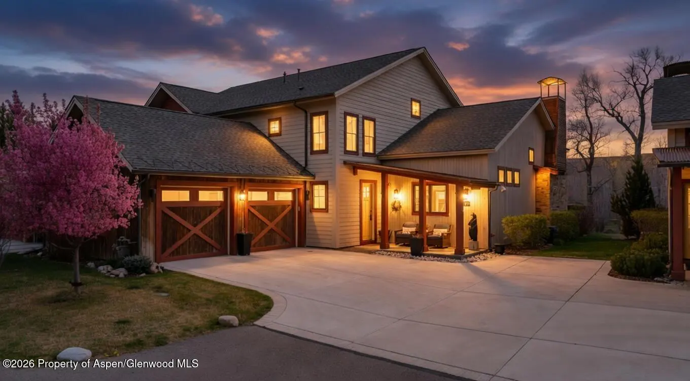 Exterior view of a two-story house with a gray roof, beige siding, and a two-car garage with wooden doors at dusk.