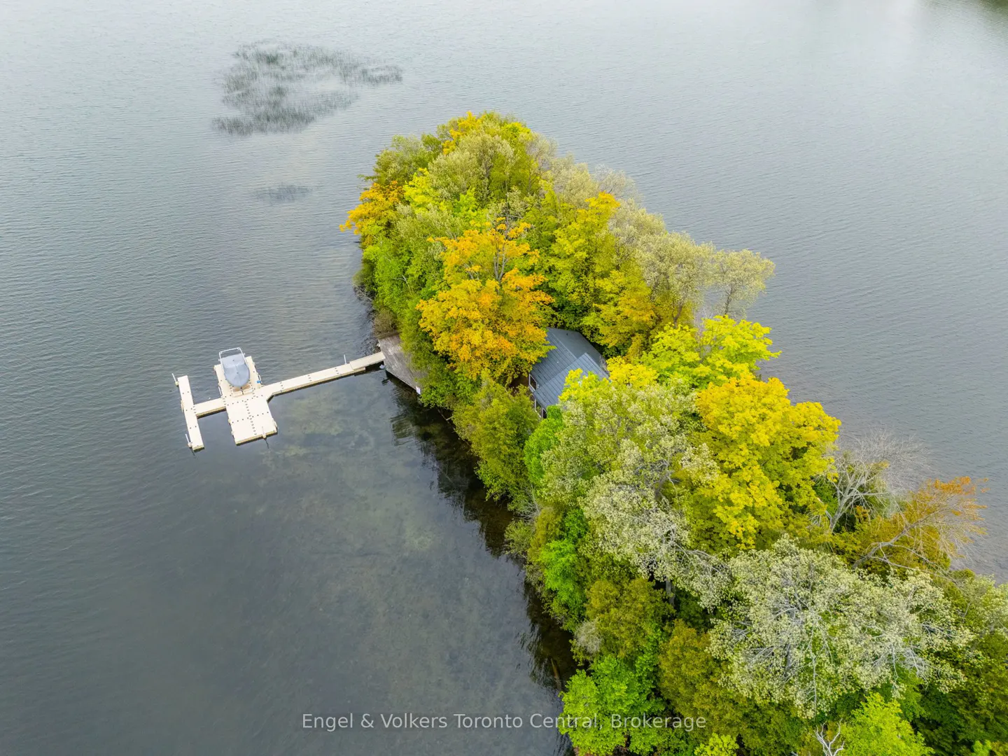 Aerial view of a small island with a house, dock, and colorful trees in a lake.