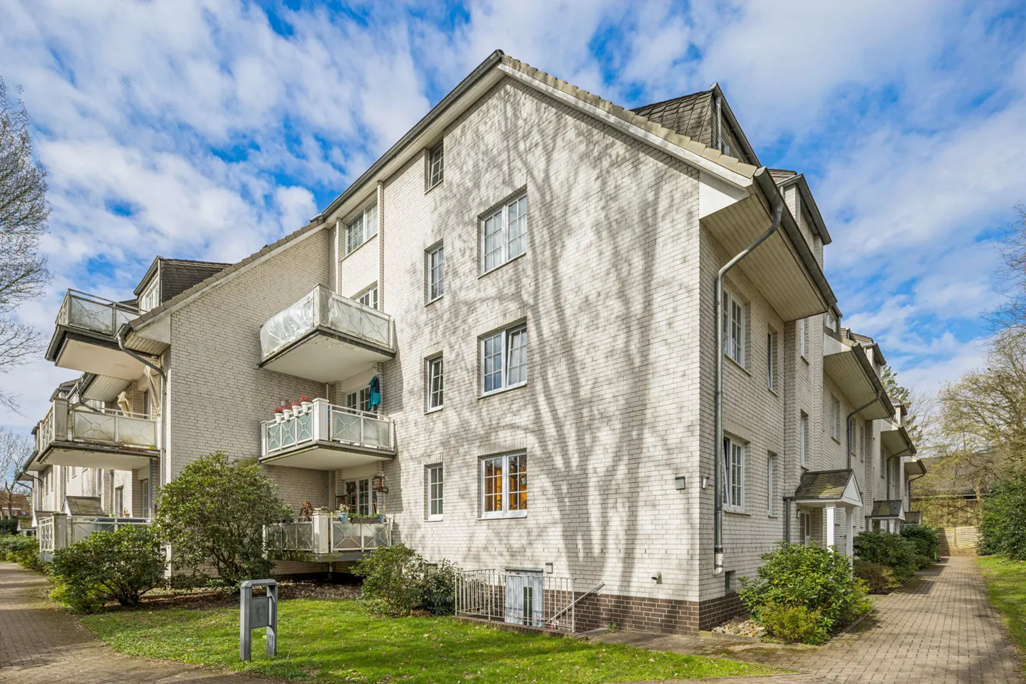Exterior view of a three-story white brick apartment building with balconies and green lawn.