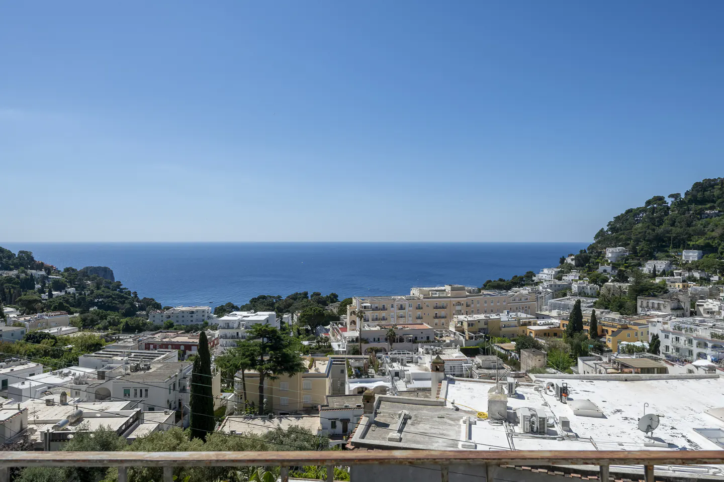 Scenic view of Capri, Italy, featuring white buildings, lush greenery, and the blue Mediterranean Sea under a clear sky.