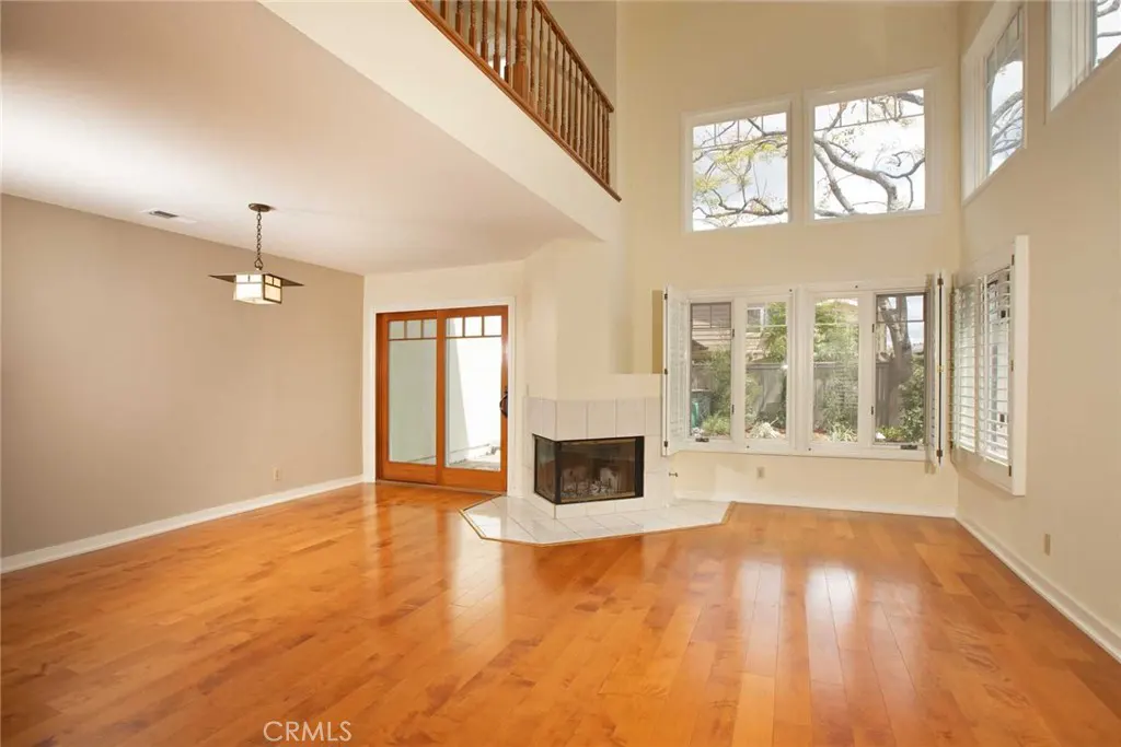 Bright, open living room with hardwood floors, fireplace, and large windows. A wooden balcony overlooks the space.