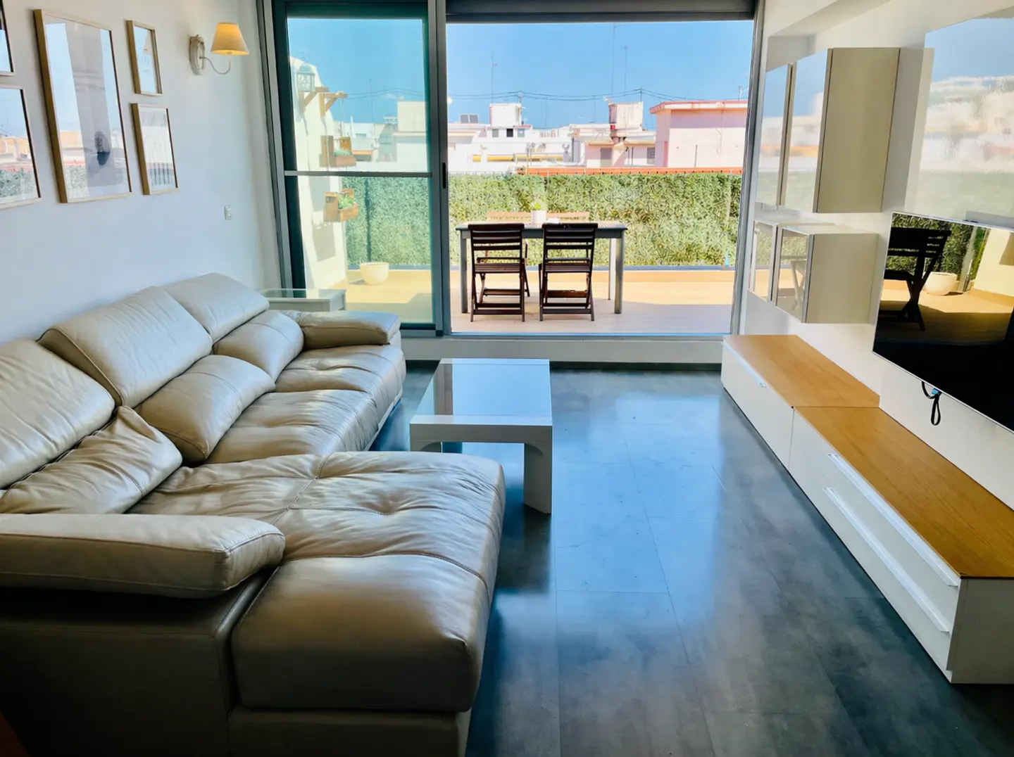 Bright living room with a beige leather sofa, white coffee table, and a balcony with outdoor furniture. Modern interior design.