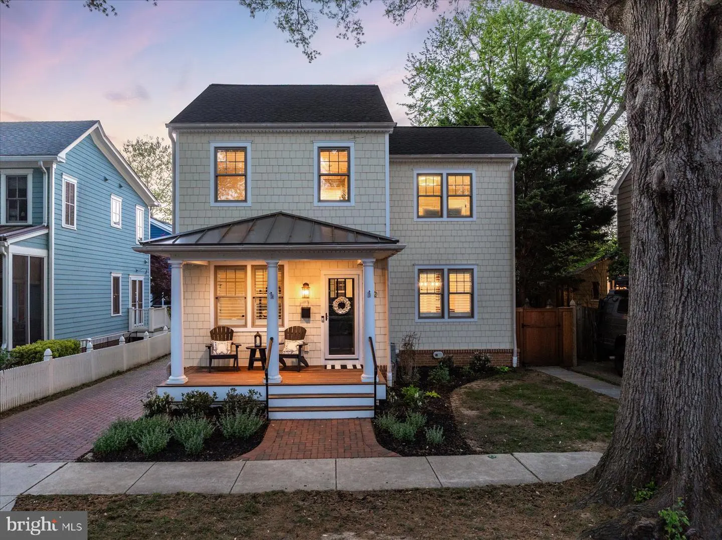 Two-story house with a porch, black roof, and beige siding. The front door has a wreath. There are two chairs on the porch.