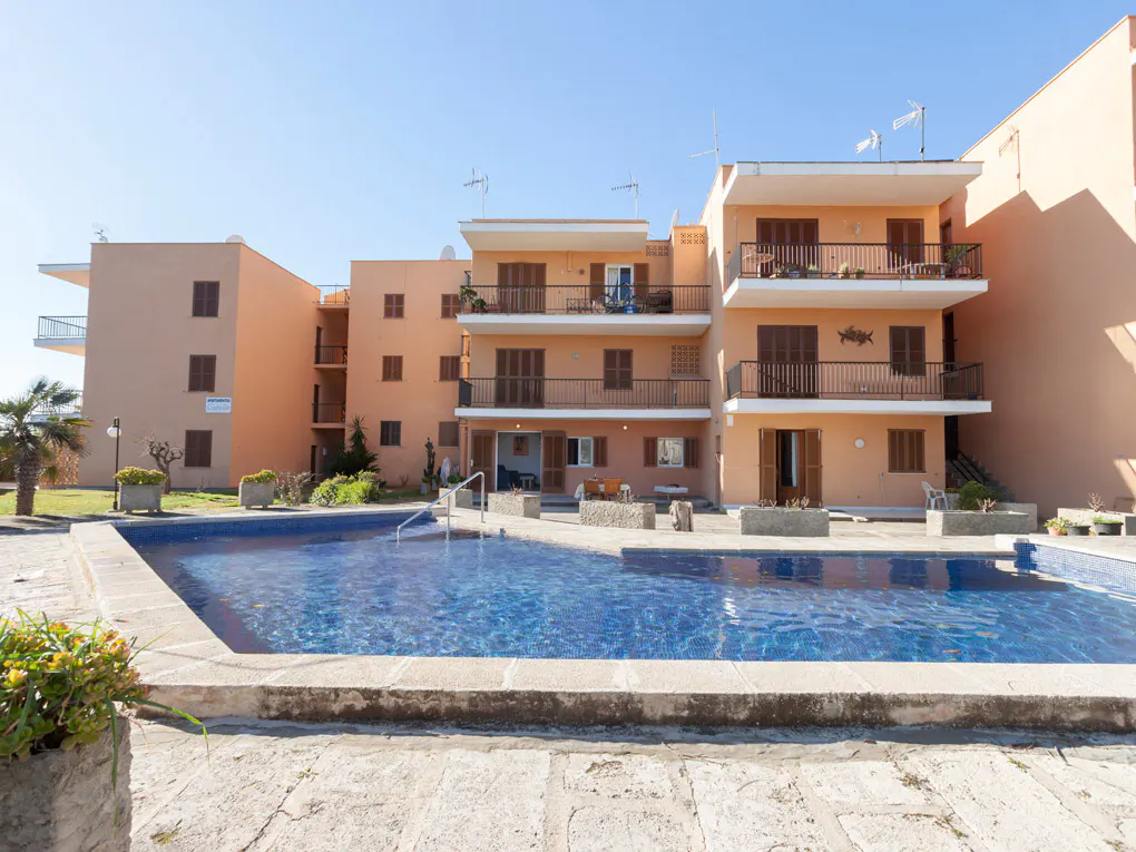 Exterior view of a peach-colored apartment complex with balconies overlooking a blue tiled swimming pool.